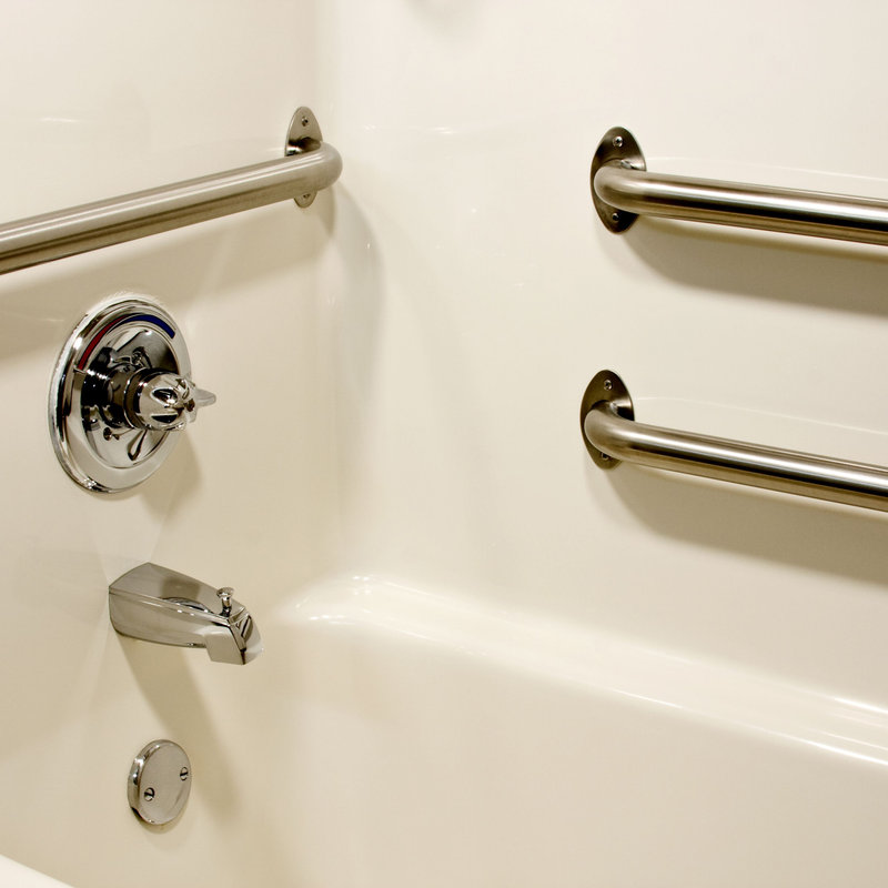 A white bathtub with three stainless steel grab bars mounted on the walls, a chrome faucet, and a control knob for the shower. The setup suggests an accessible or safety-conscious bathroom design.