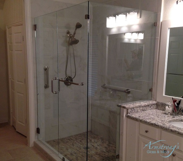 A bathroom with a large glass-enclosed shower, granite countertop vanity, wall-mounted lights above the mirror, and neutral-colored tile flooring. The room looks clean and modern.